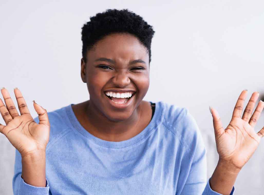 A casual young African American woman laughing with her hands up in celebration with her significant weight loss